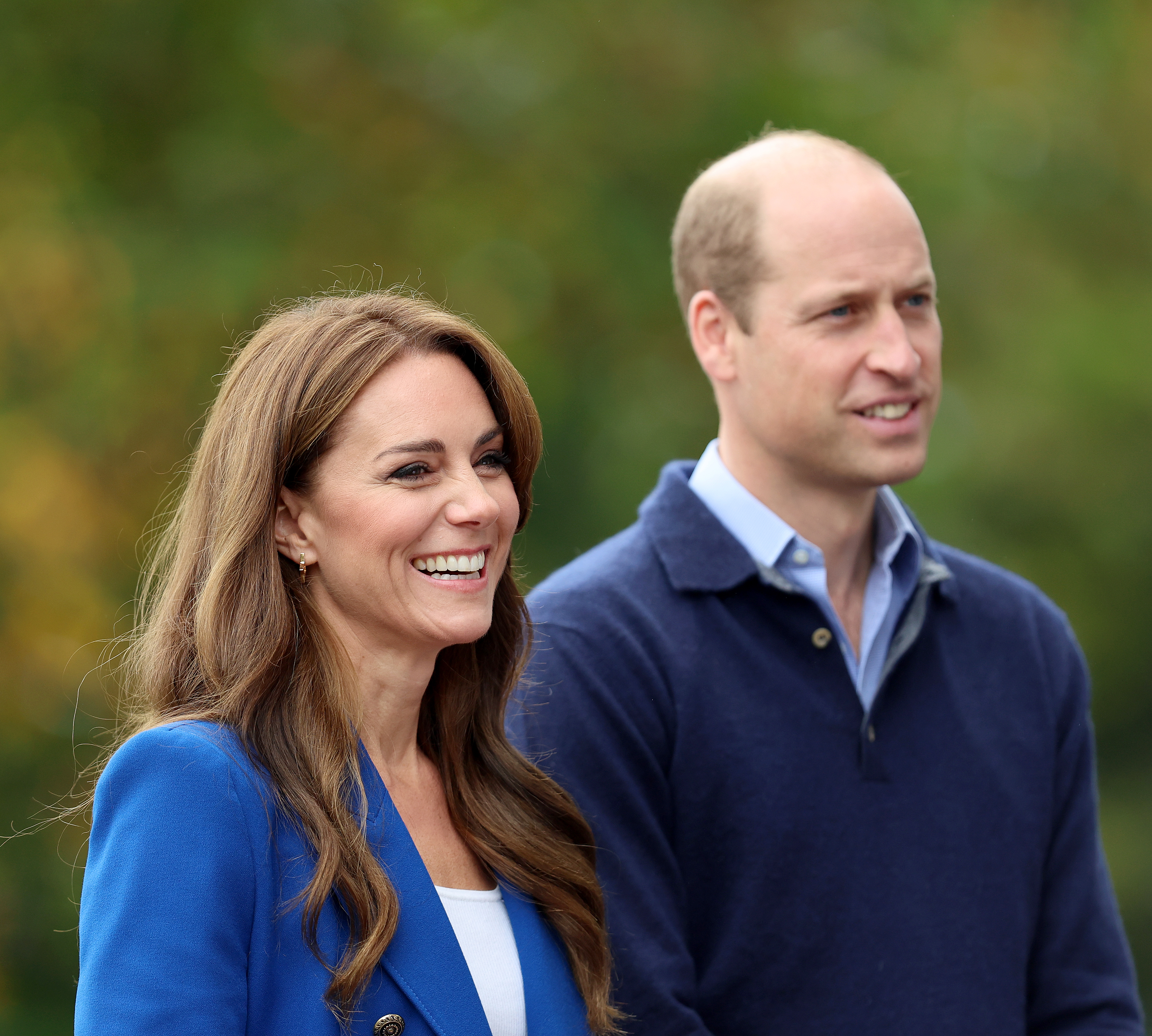 Kate Middleton and Prince William smiling, in casual attire, outdoors; Kate wears a blue blazer, William in a collared shirt