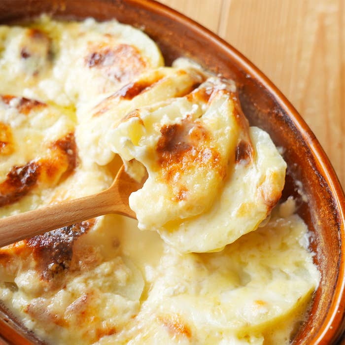 焼きたてのチーズがトッピングされたポテトグラタン。木製スプーンで一部が盛り付けられている。