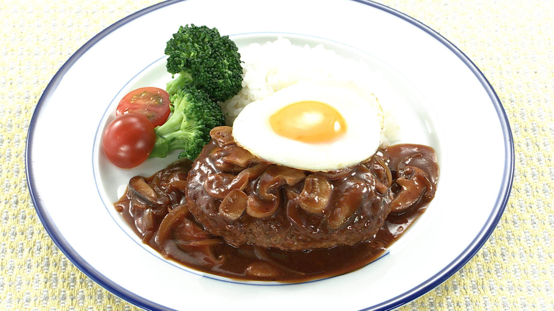 皿に盛られたハンバーグステーキ、目玉焼き、ブロッコリー、トマトです。