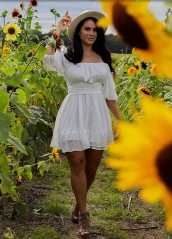 Reviewer in a white dress with a hat poses among sunflowers