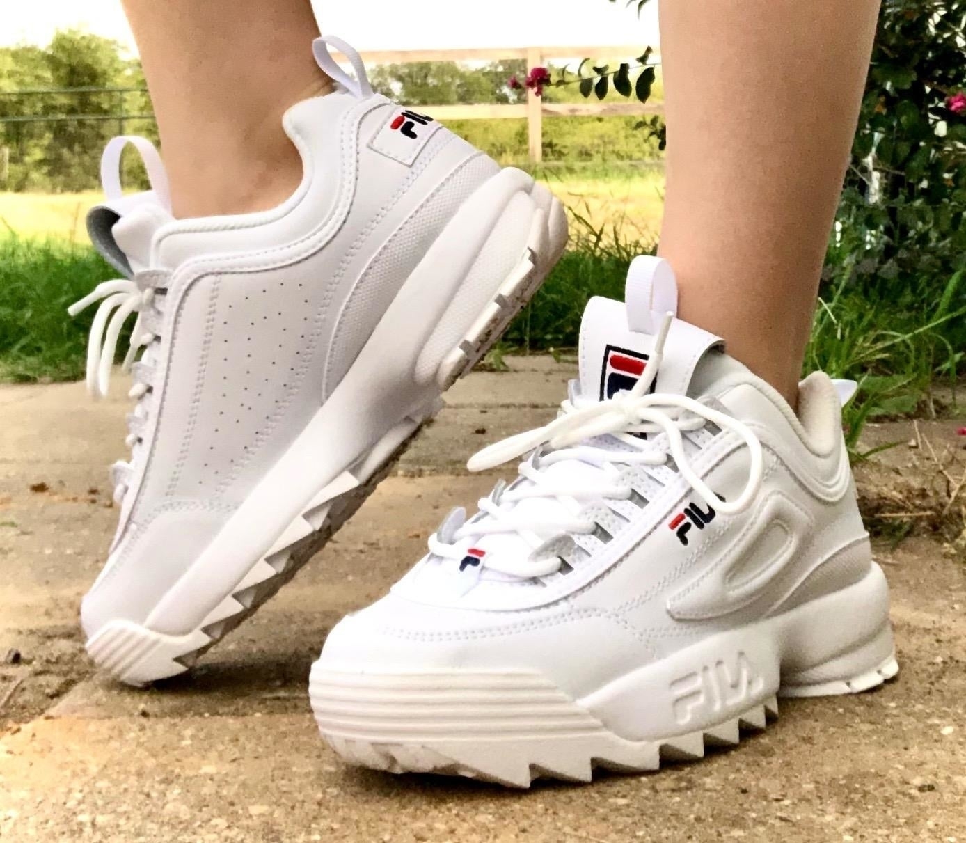 Person wearing white FILA sneakers with chunky soles, standing on grass