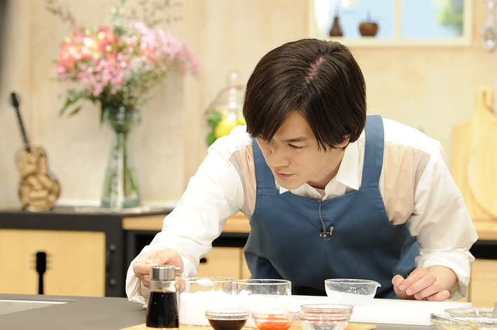 エプロンをつけた男性が調理台で料理の準備をしている様子です。