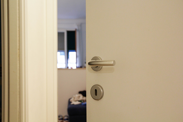 開いているドアのドアノブ、部屋の中にはぼんやりと物が見える。