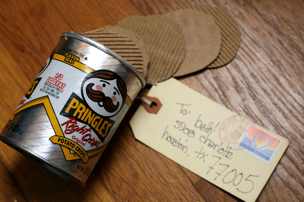 A Pringles can on a wooden surface with a gift tag addressed to &quot;Ben&quot; with &quot;5000 charlote houston tx 77005&quot; handwritten on it