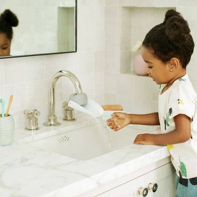 Child washes hands at sink, reflected in mirror, wearing a printed tee