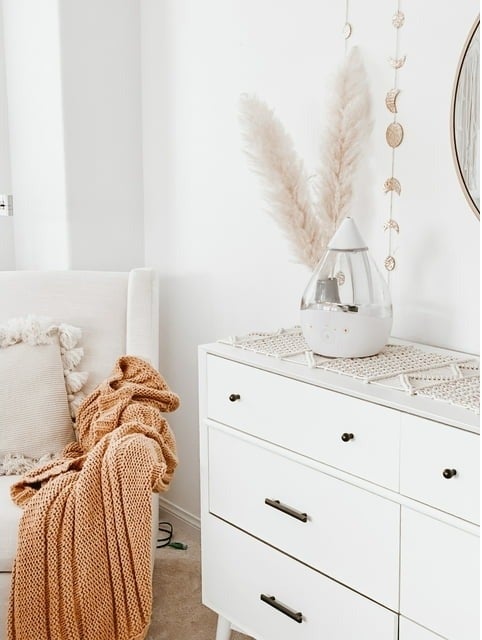 Cozy room corner with a white dresser, a draped knitted throw, and decorative items on display