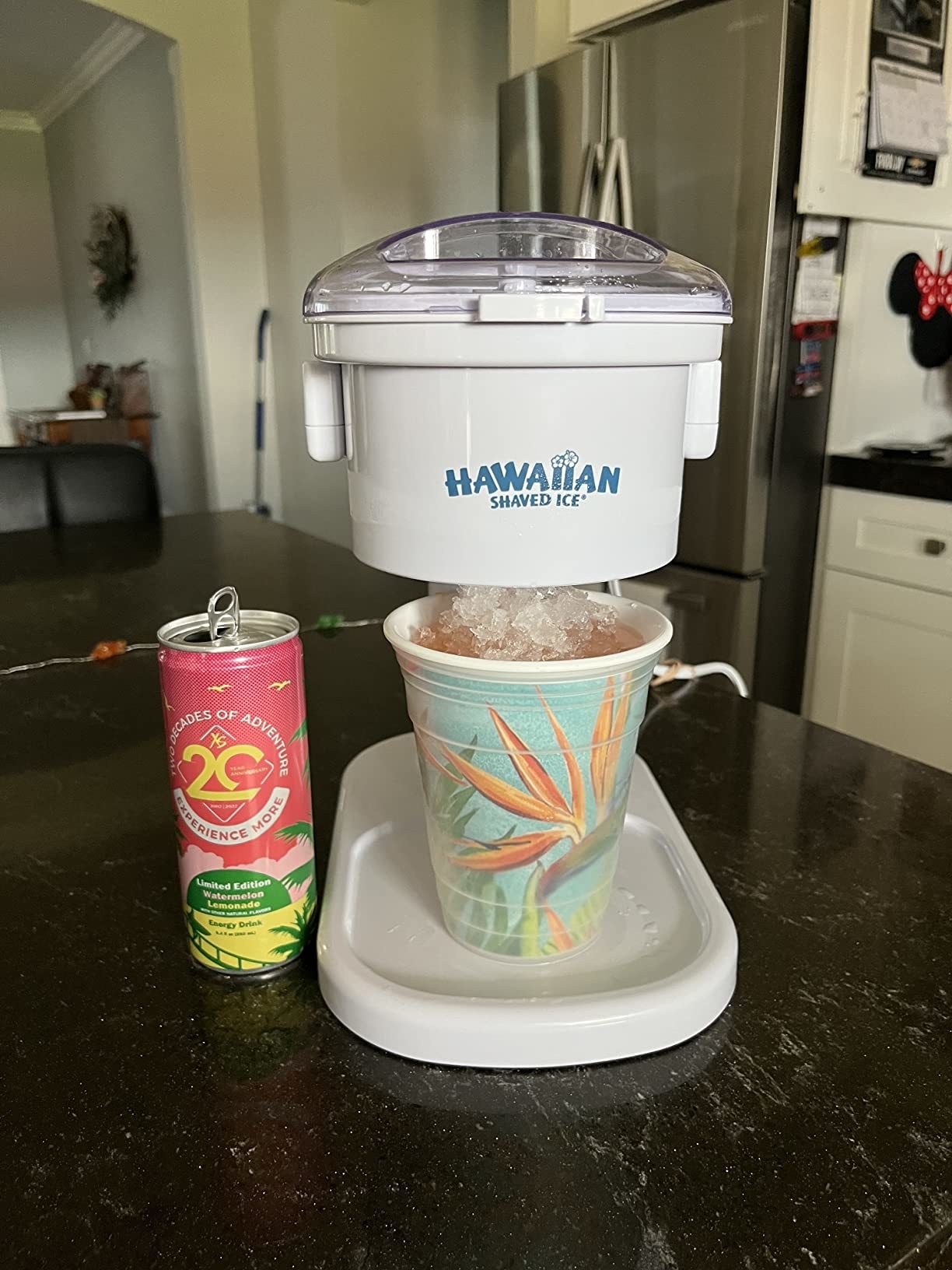 Hawaiian Shaved Ice machine with a can of juice and a cup filled with shaved ice on a kitchen counter
