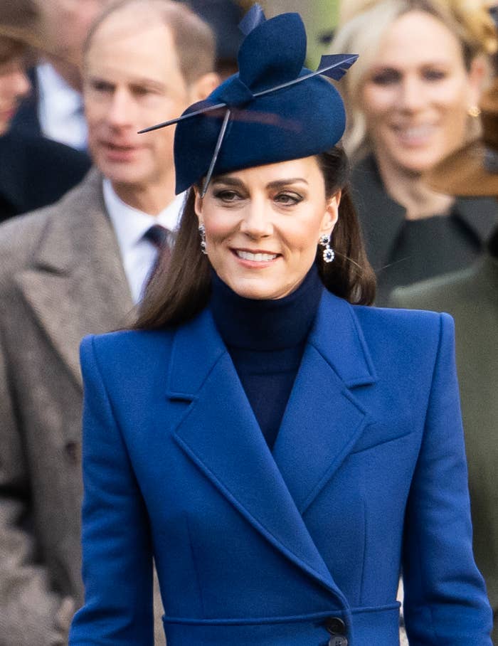 Woman in elegant blue coat and matching hat, accessorized with earrings, attending a formal event
