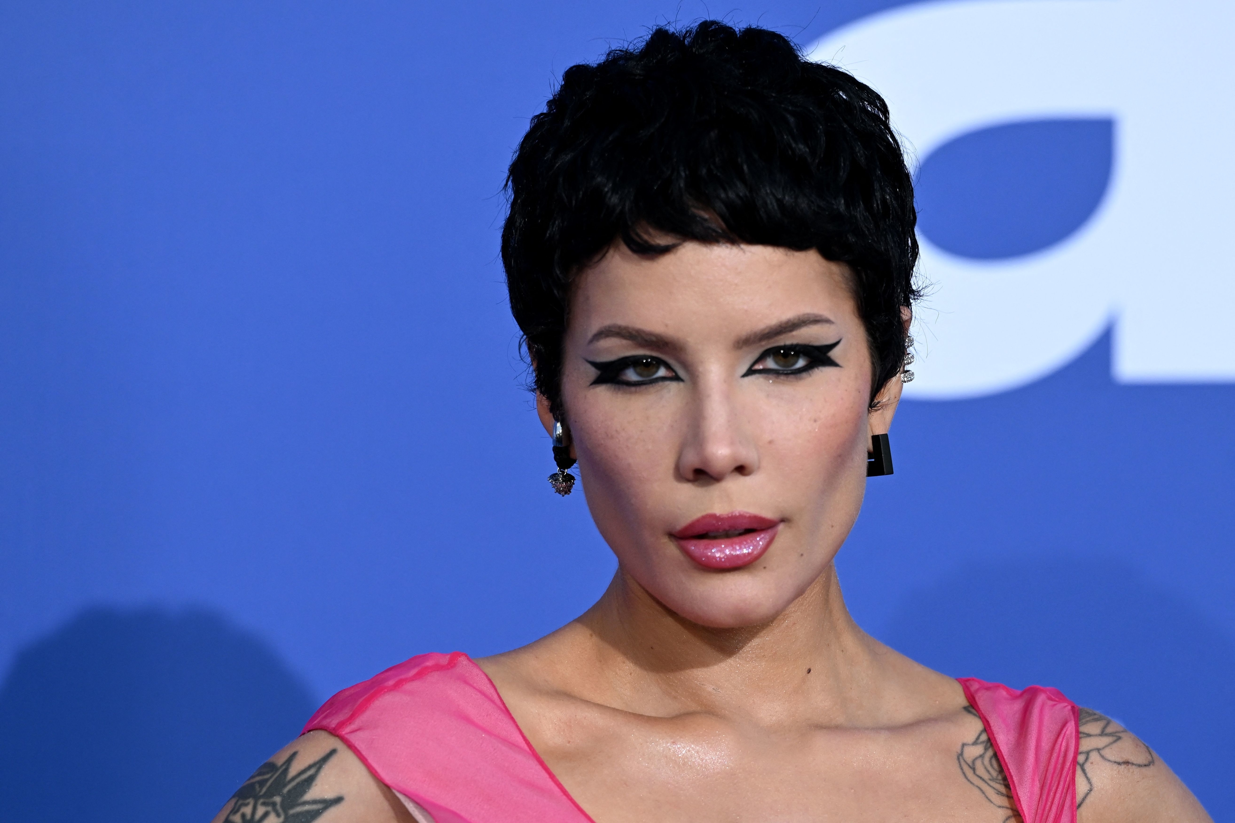 Halsey poses with short hair, winged eyeliner, and a pink top at an event