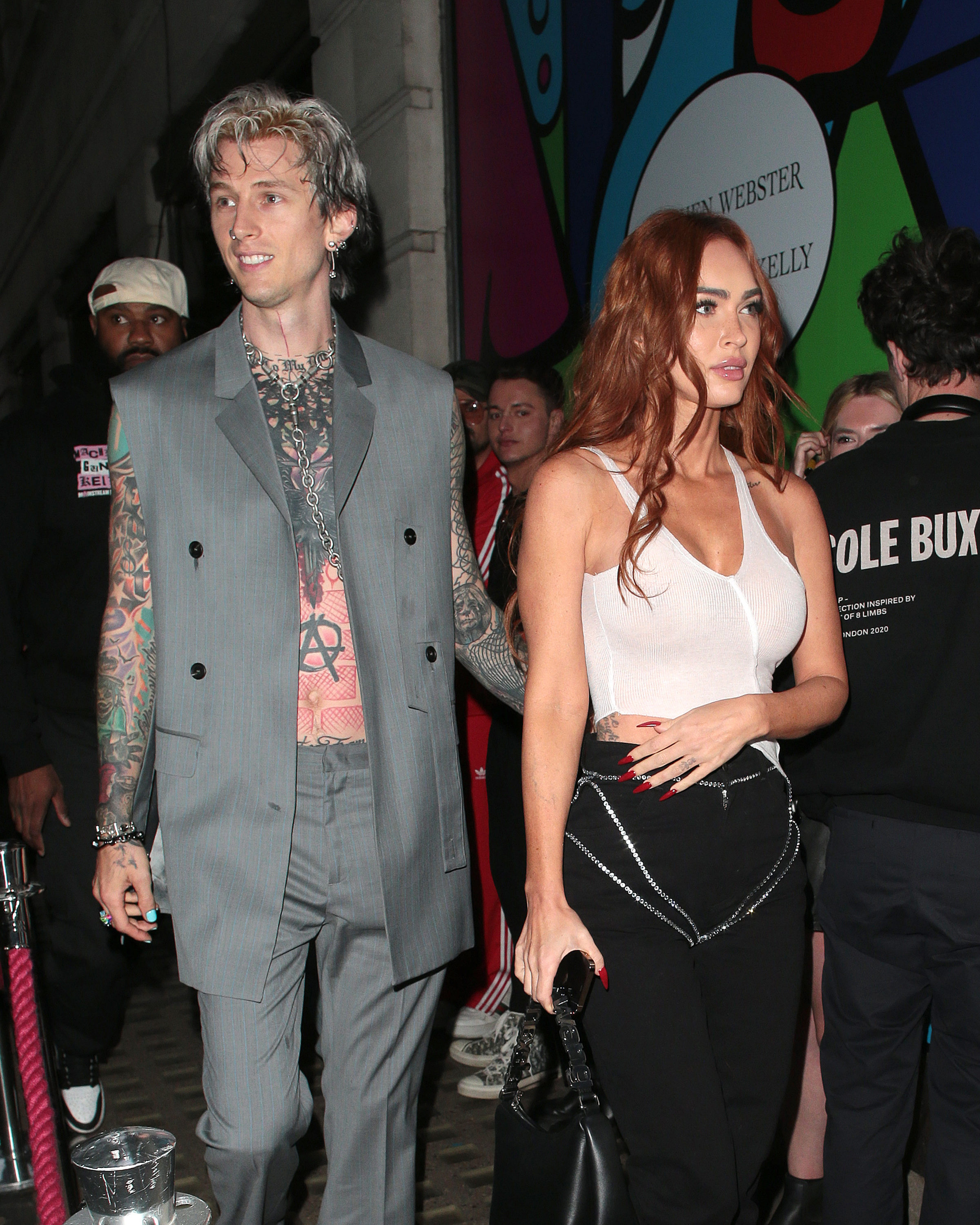 the two at an event, MGK wearing a vest suit with no shirt and Megan in a skirt and sheer top