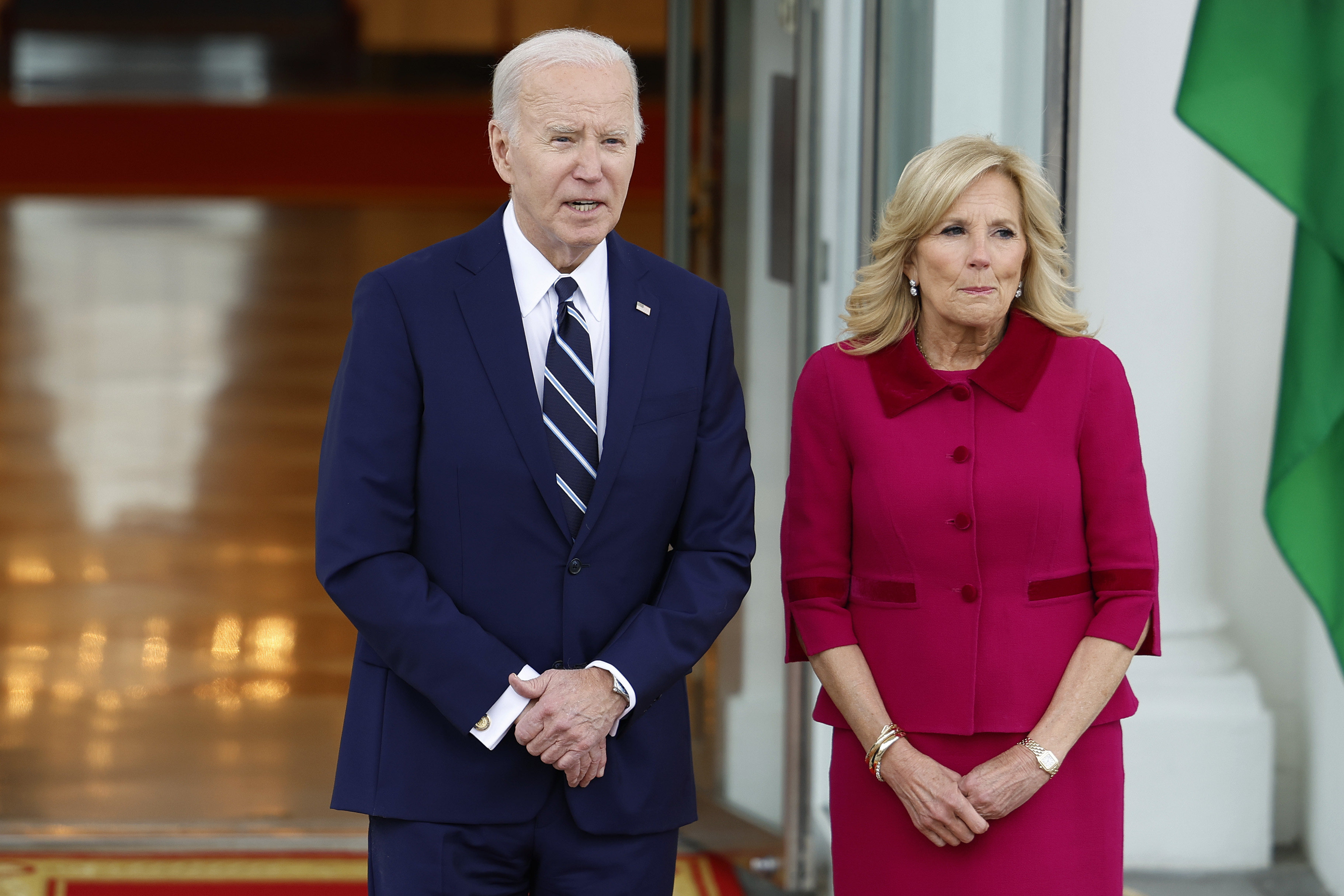 Joe Biden and Jill Biden standing together, Joe in a suit with a tie and Jill in a green dress and jacket