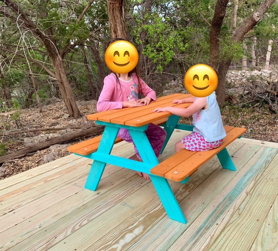 Two children sitting at a brightly painted turquoise picnic table in a natural setting