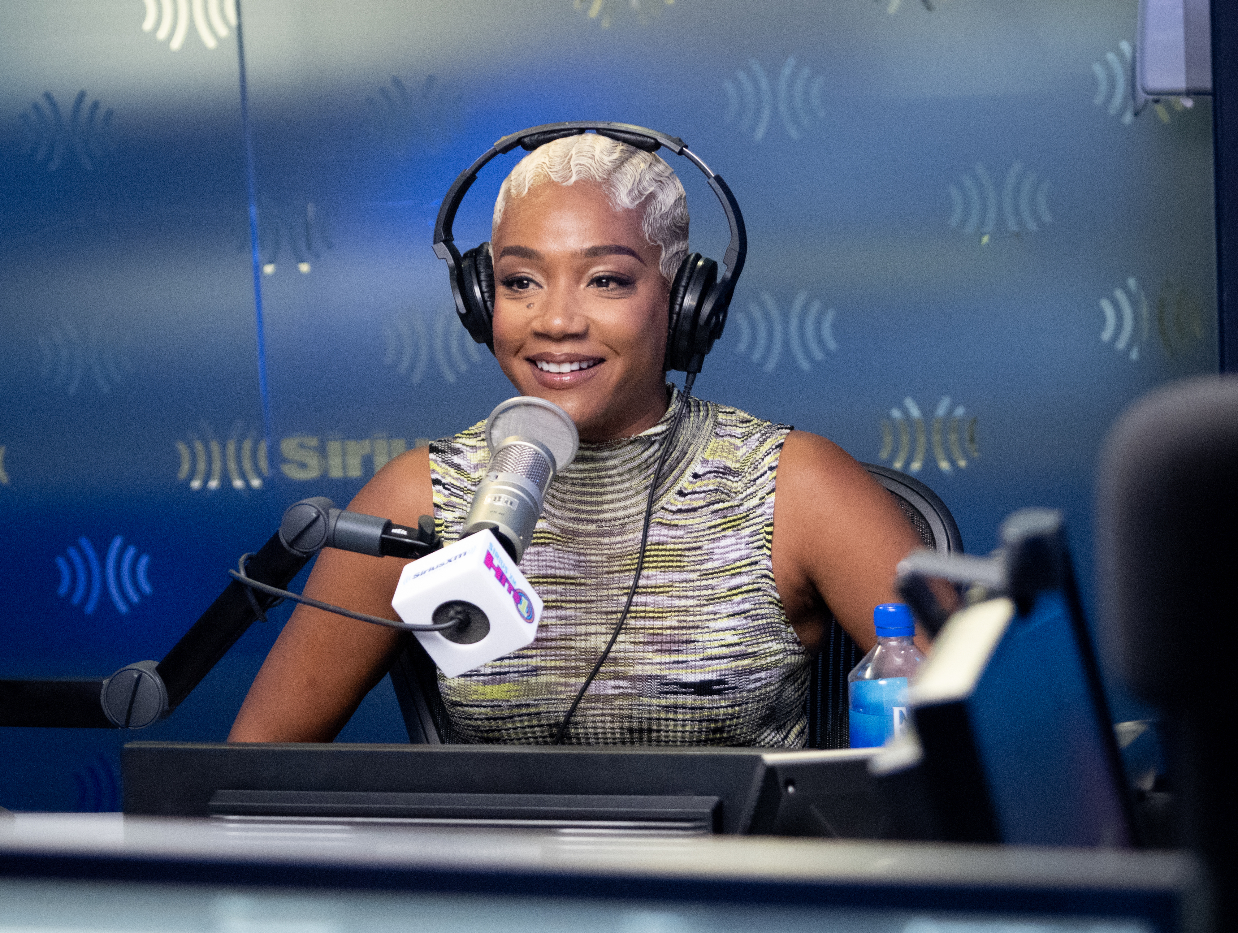 Tiffany Haddish wearing a sparkly sleeveless top, speaking into a microphone during a radio show interview