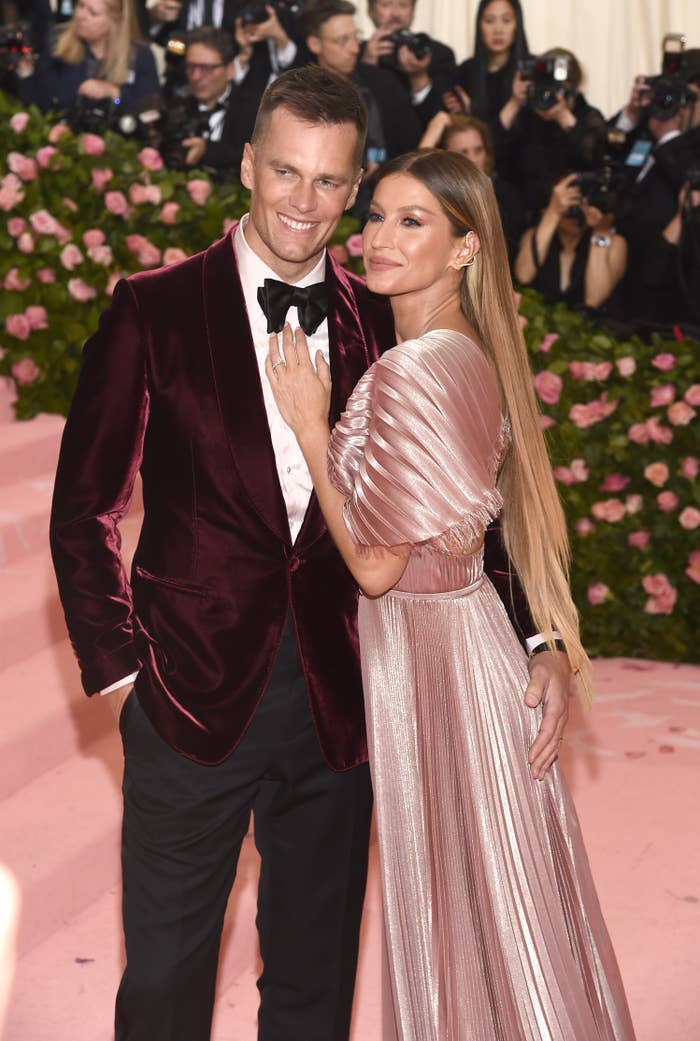 Tom Brady and Gisele Bündchen posing together; he&#x27;s in a velvet suit and she&#x27;s wearing a metallic gown