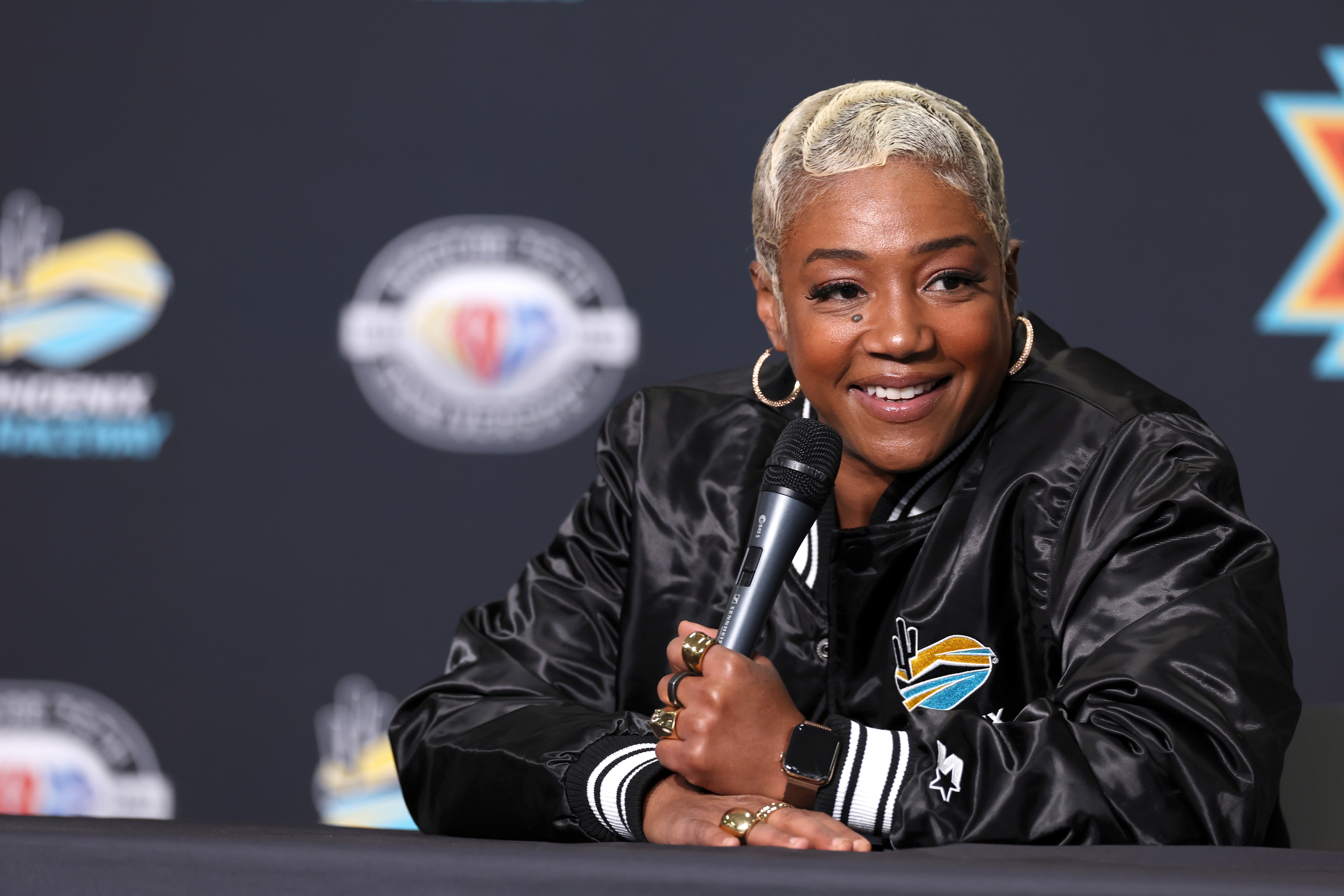 Tiffany Haddish answering questions at an event, wearing a black sports jacket with emblem