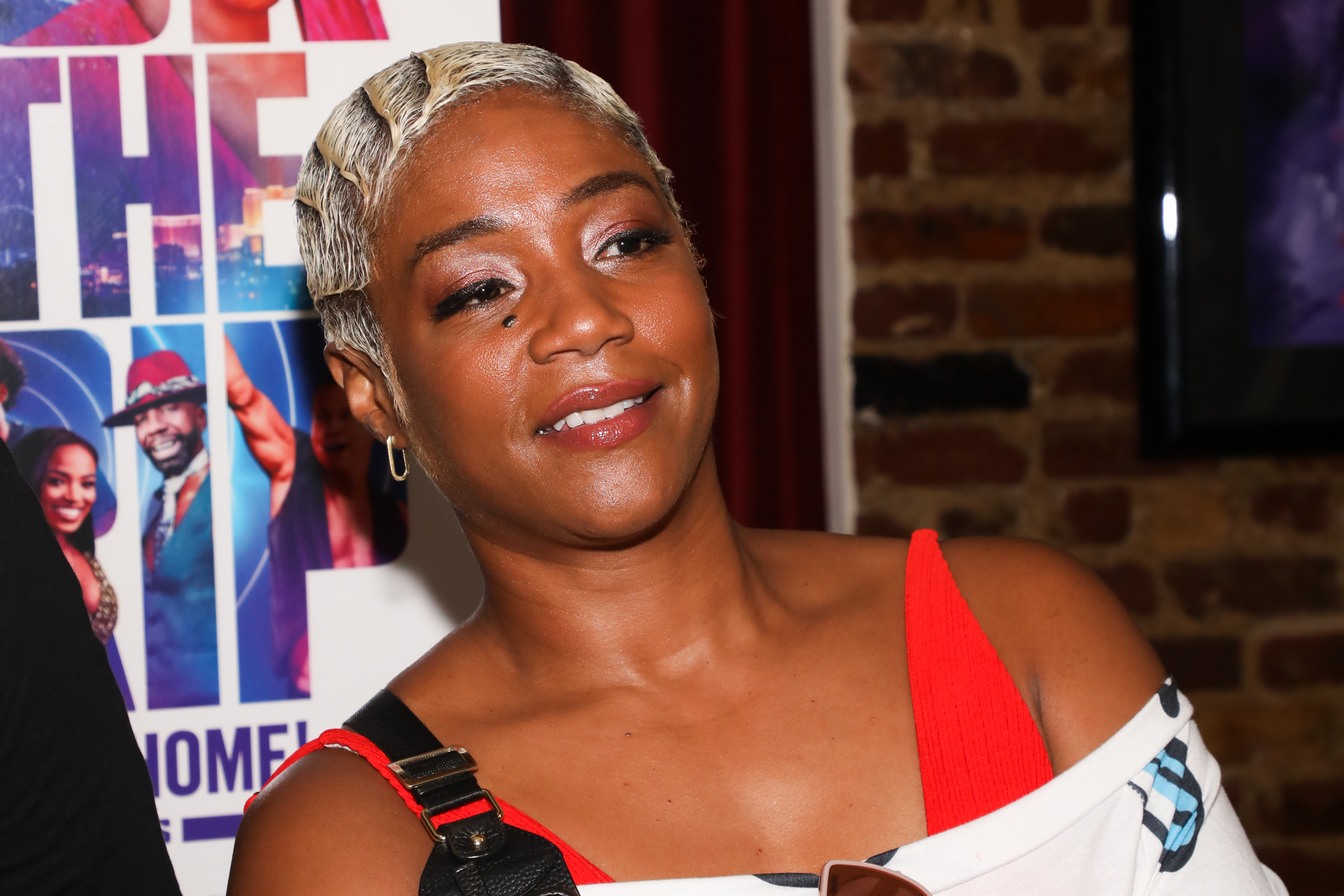 Tiffany Haddish poses in a white dress with red straps at an event