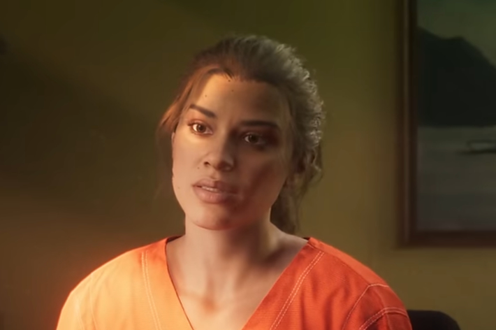 Woman in orange prison attire sitting, looking concerned. Appears in a drama scene