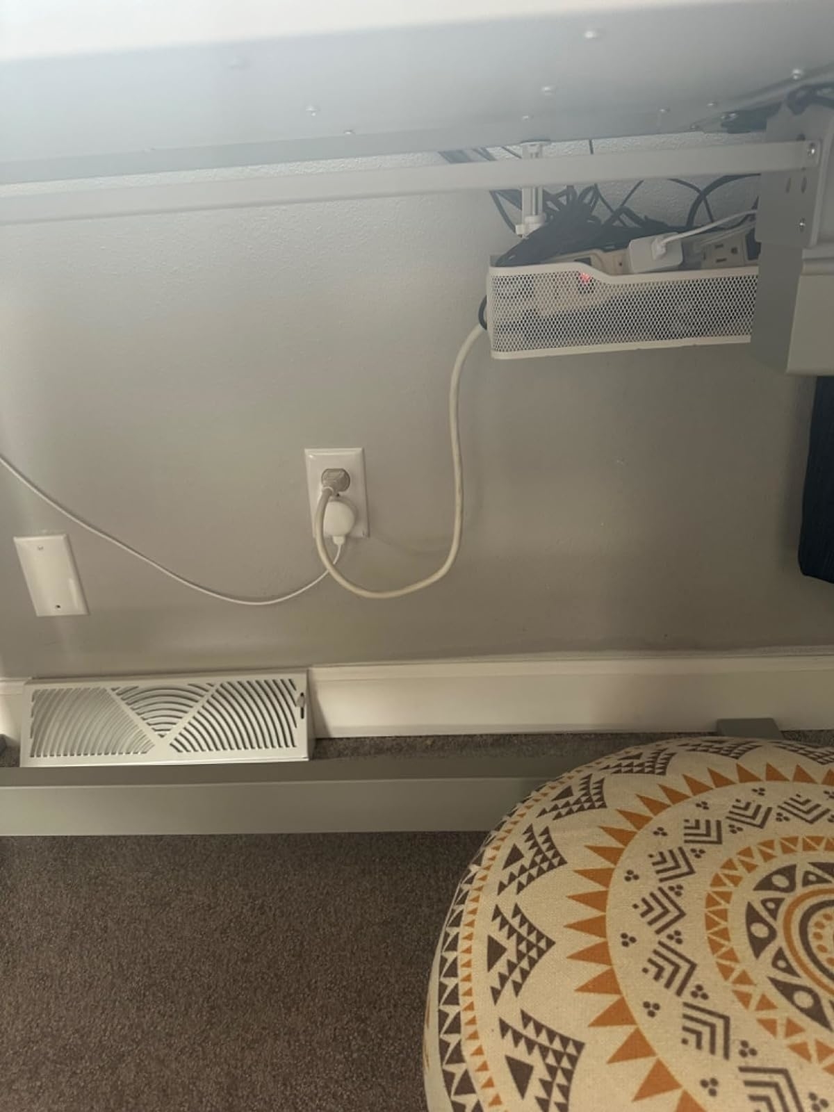 Power strip and cables organized under a desk next to a patterned ottoman