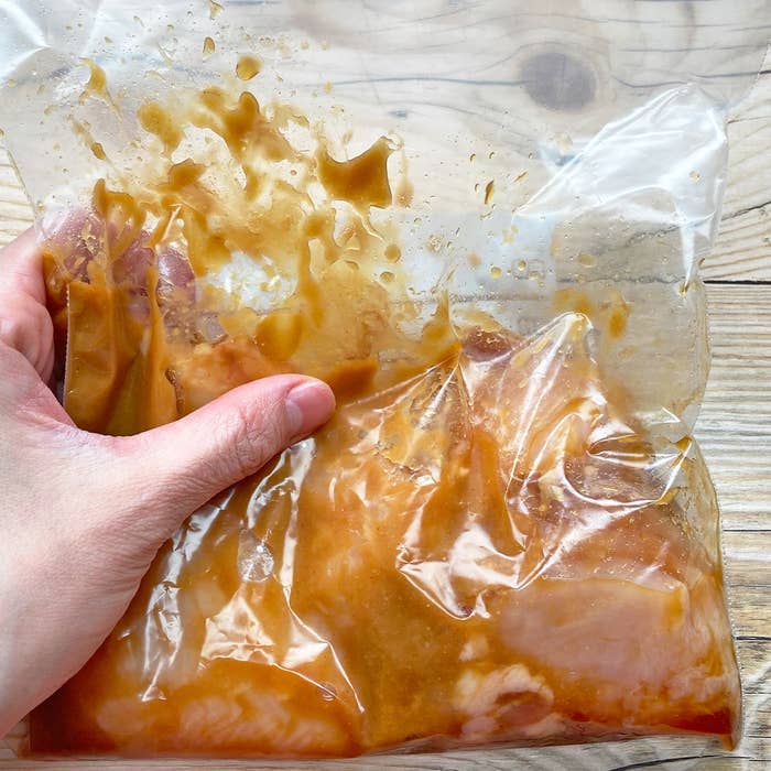 手が袋を持っていて、中には液体が含まれた鶏むね肉が入っています。