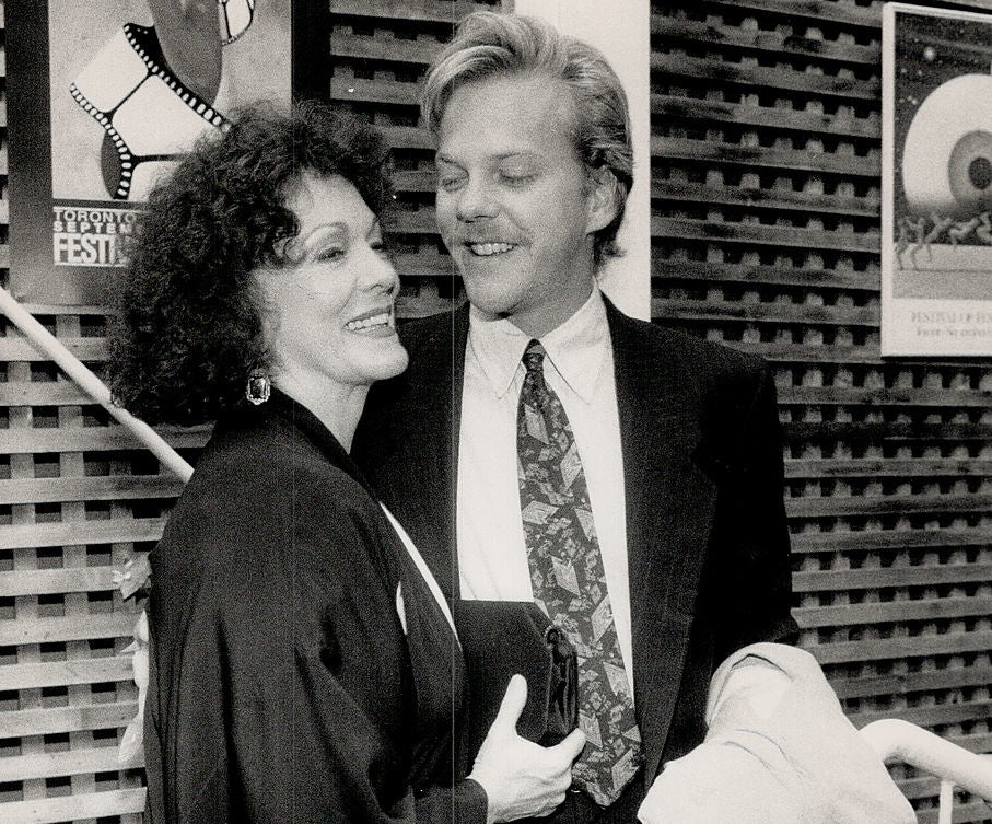 Shirley smiling in a black robe with a floral accent, and Kiefer in a suit and tie, holding a jacket