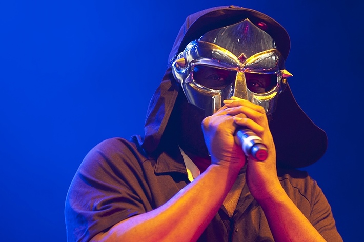 Performer on stage wearing a distinctive mask and holding a microphone