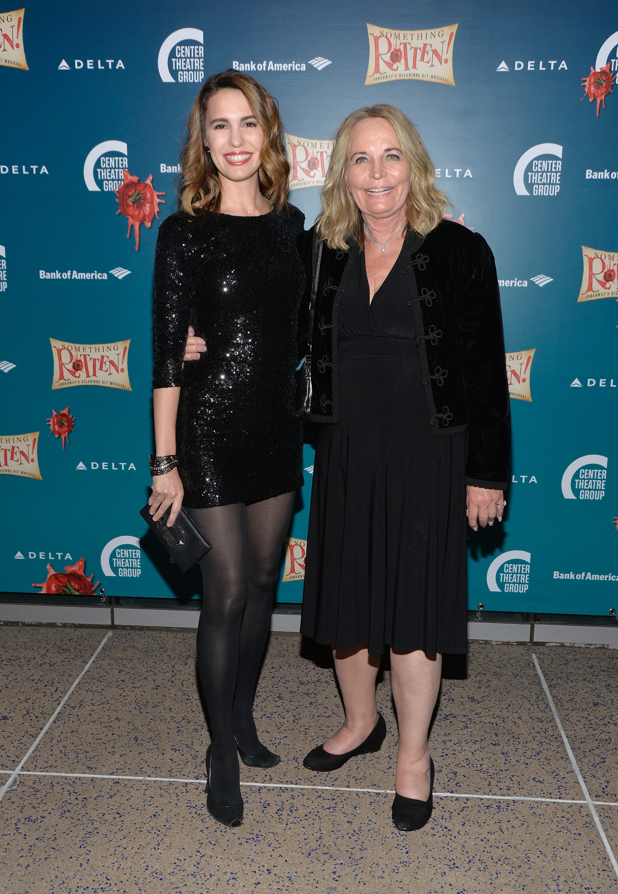 Christy in a sparkly black minidress and tights, with Sharon, in a black dress and patterned jacket, at a media event