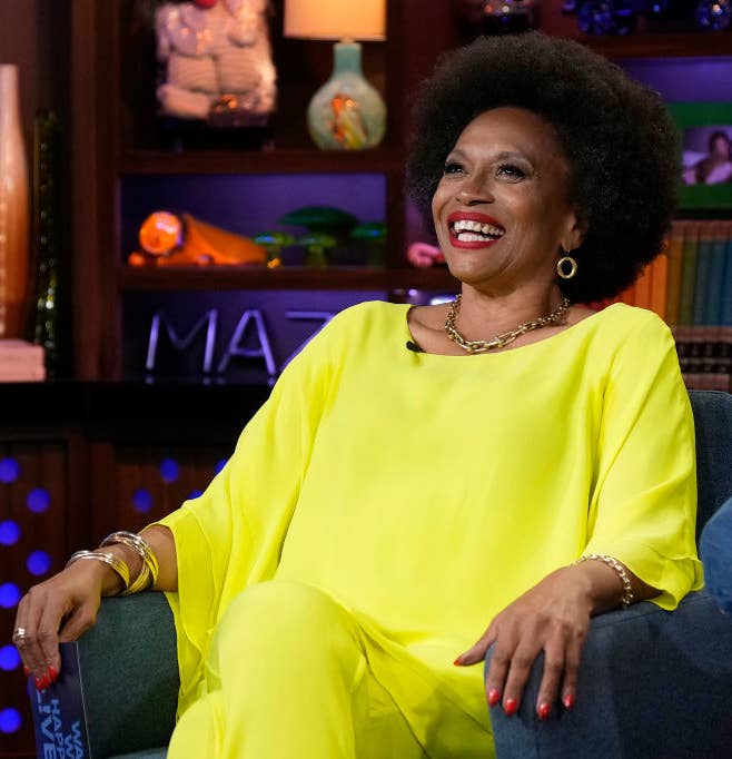 Jenifer Lewis in a bright outfit sitting with a wide smile on a talk show set
