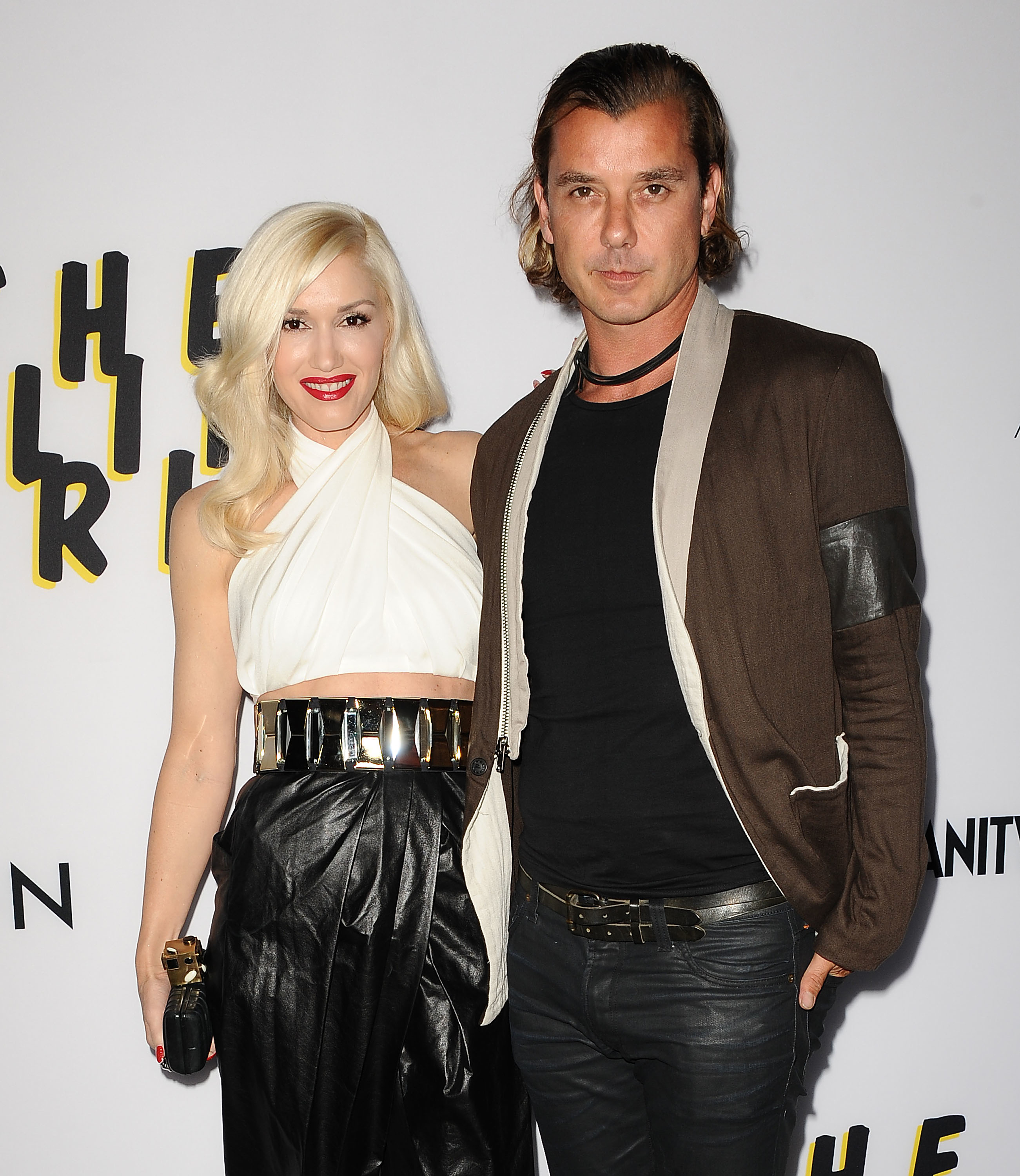 Gwen Stefani and Gavin Rossdale pose together; Stefani in a white top and black skirt, Rossdale in a brown jacket and black shirt