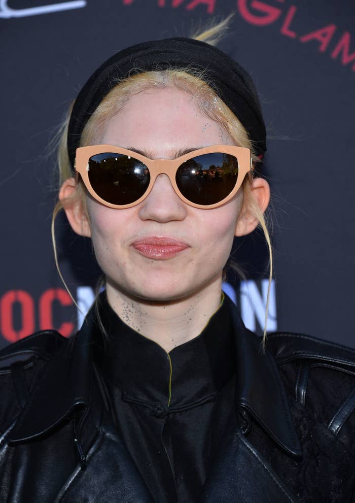 Grimes wearing large sunglasses, headband, and leather jacket at an event