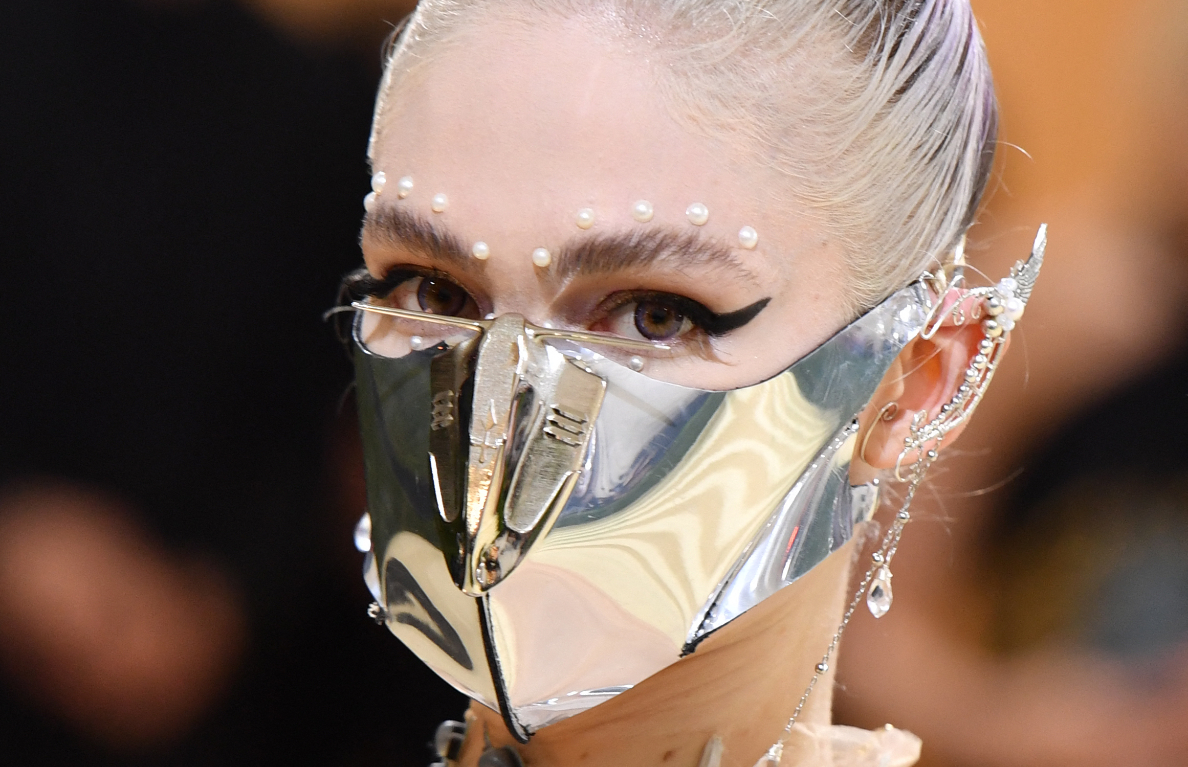 Grimes wearing a metallic mask with pearl adornments on their forehead