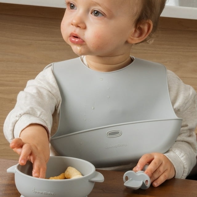 Toddler wearing a bib using a bowl and utensil, with silicone suction product visible