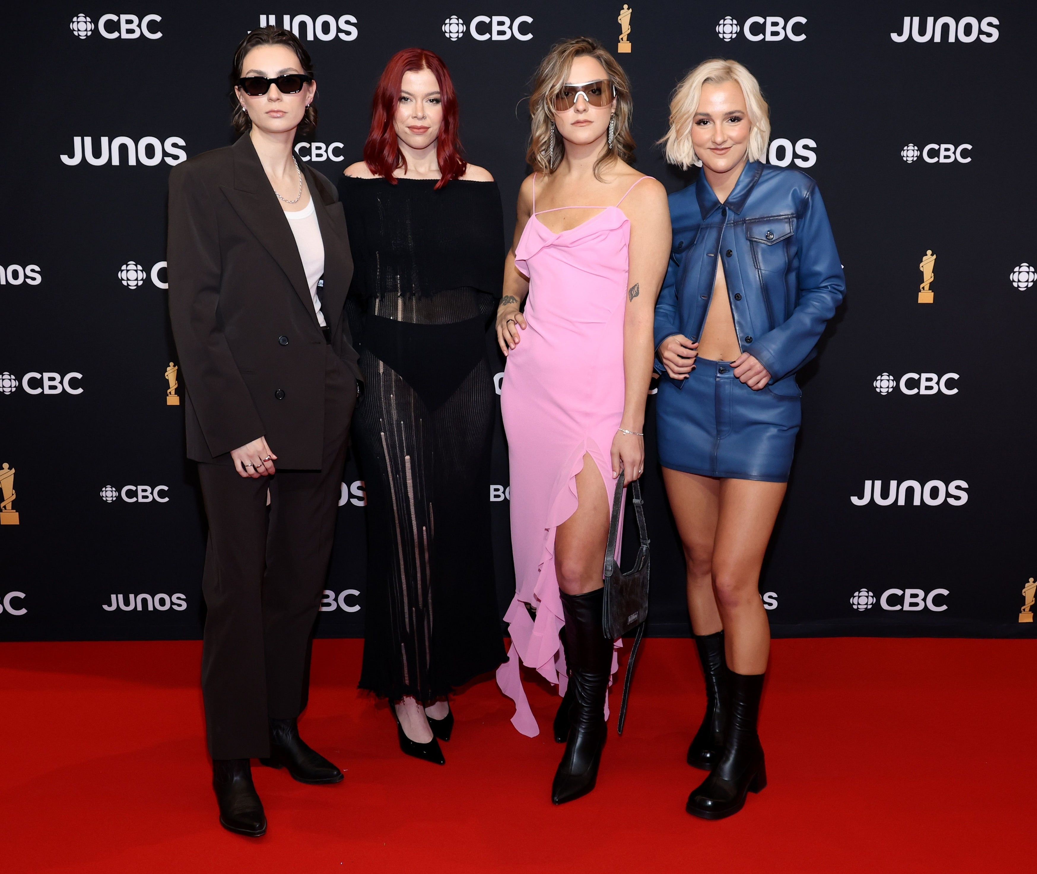 Four women posing at an event, dressed in stylish attire ranging from suits to dresses