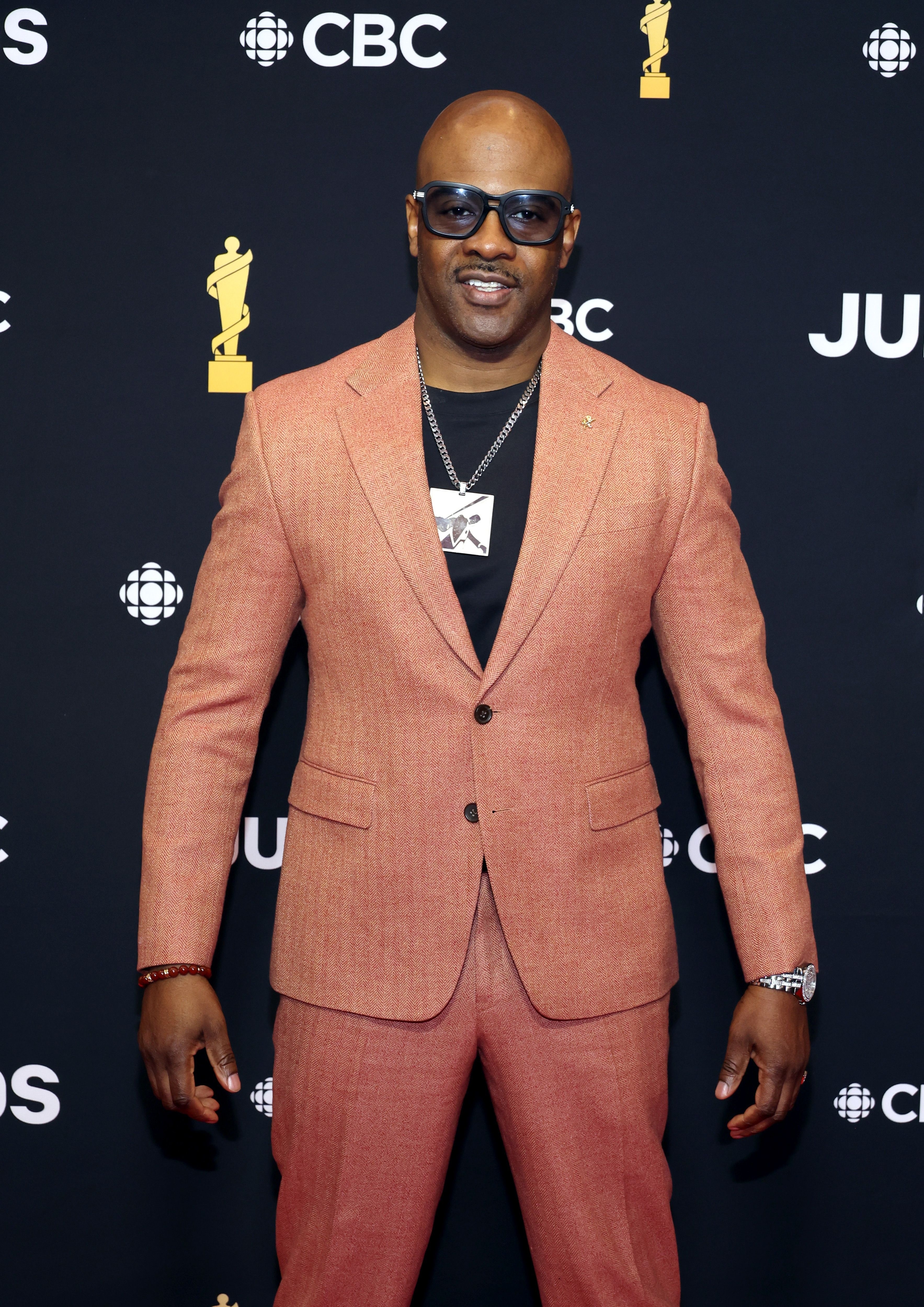 Man in a peach suit poses with sunglasses at an event with CBC backdrop