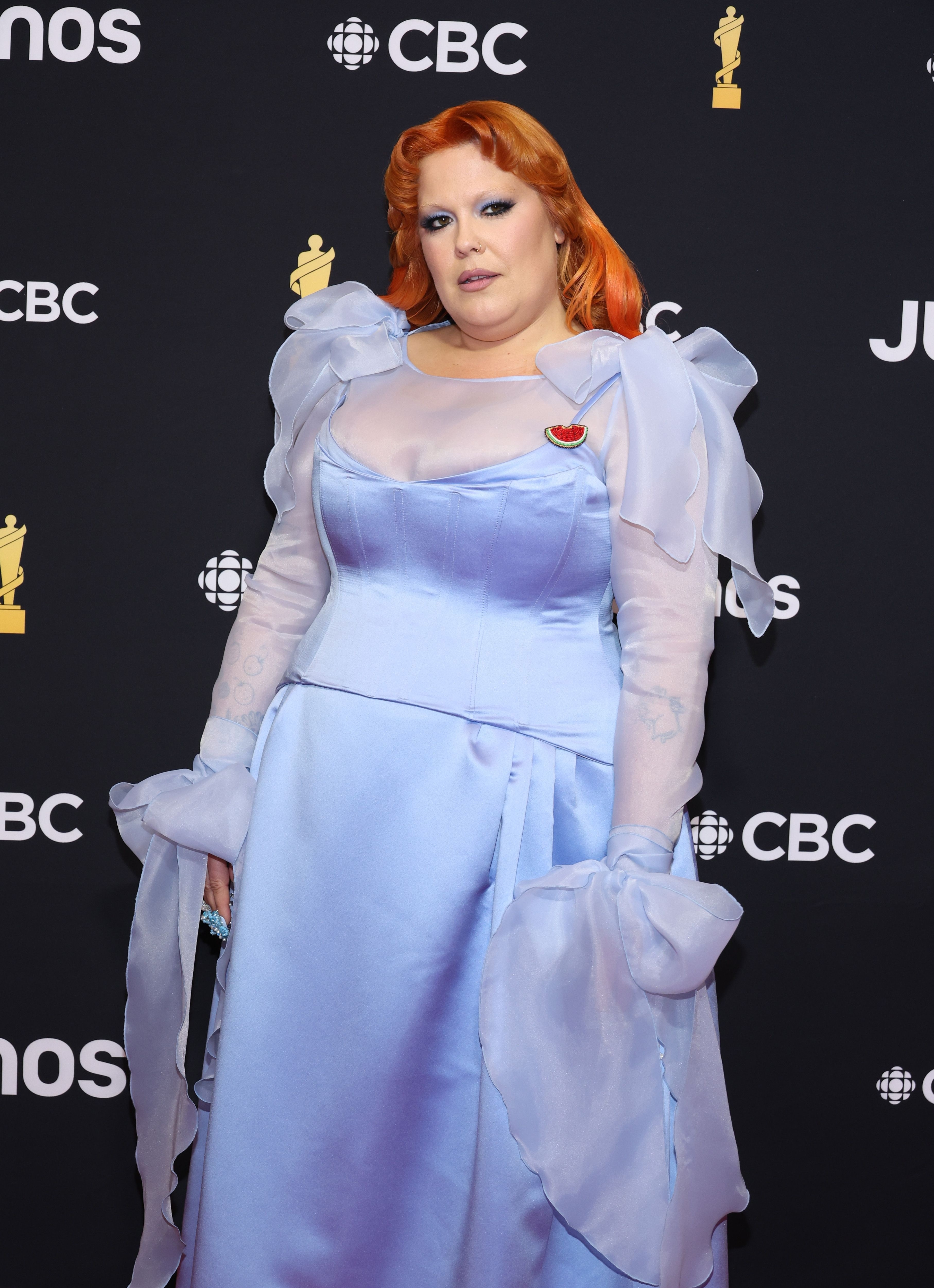 Person posing in a blue gown with sheer sleeves and ruffle details, sporting red hair