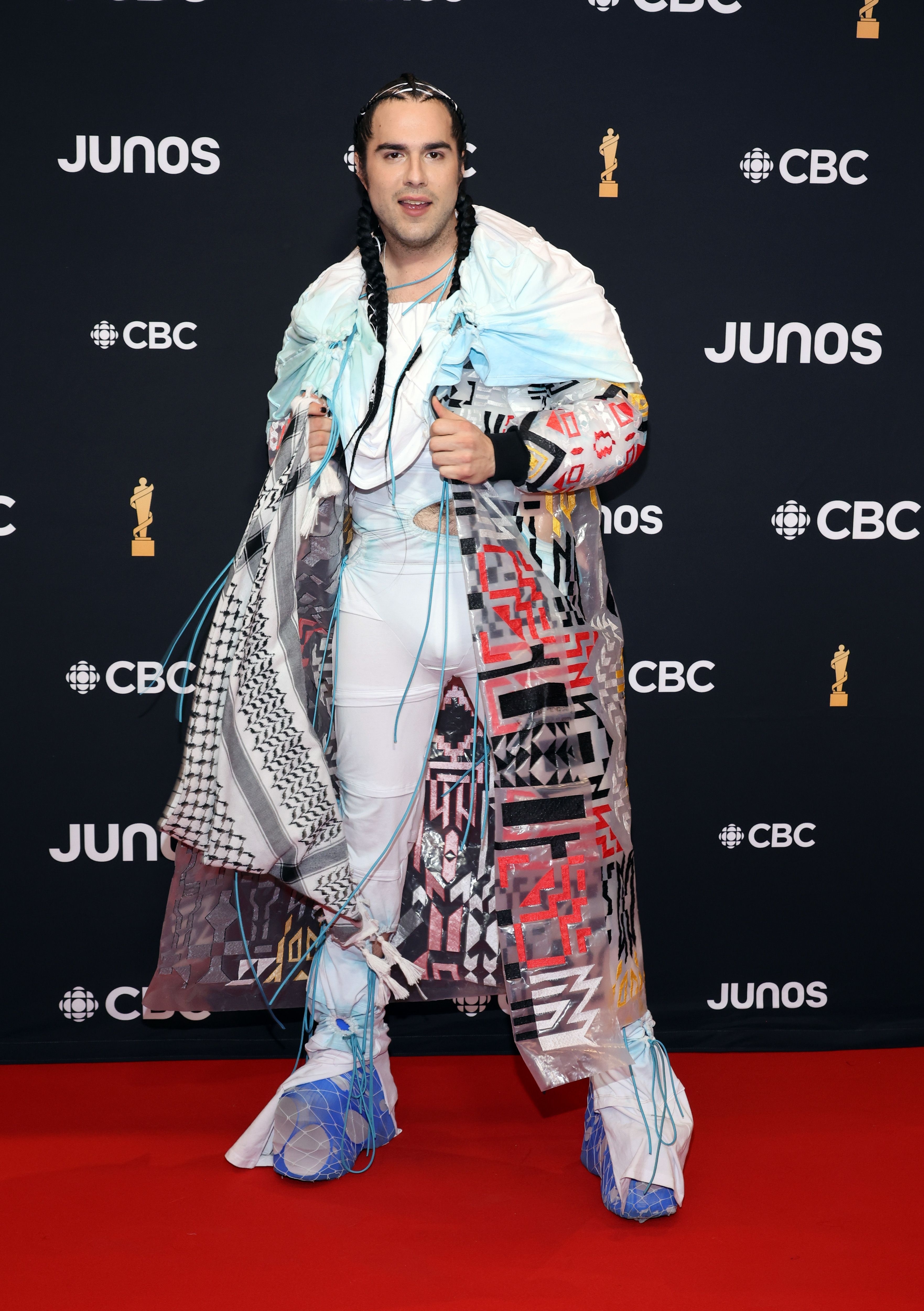 Person on red carpet in eclectic outfit with mixed patterns and layered white jacket