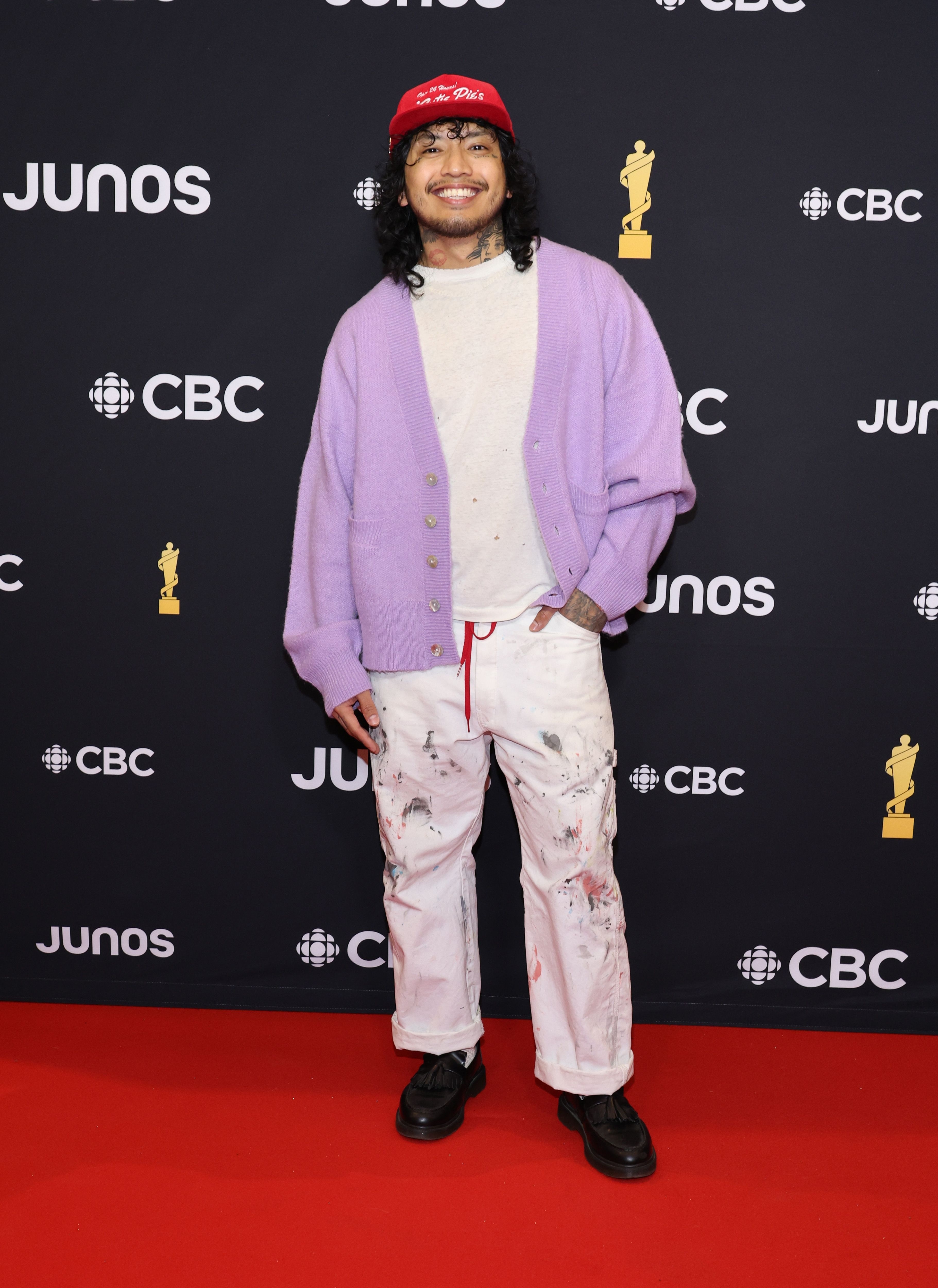 Man in a purple cardigan, white splattered pants, red bandana, posing at the Junos