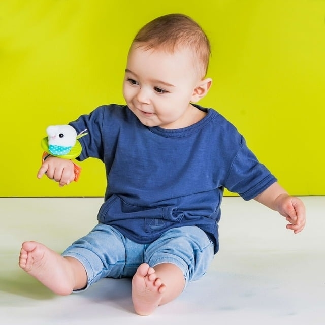 Baby in a casual outfit playing with a rattle attached to its wrist.