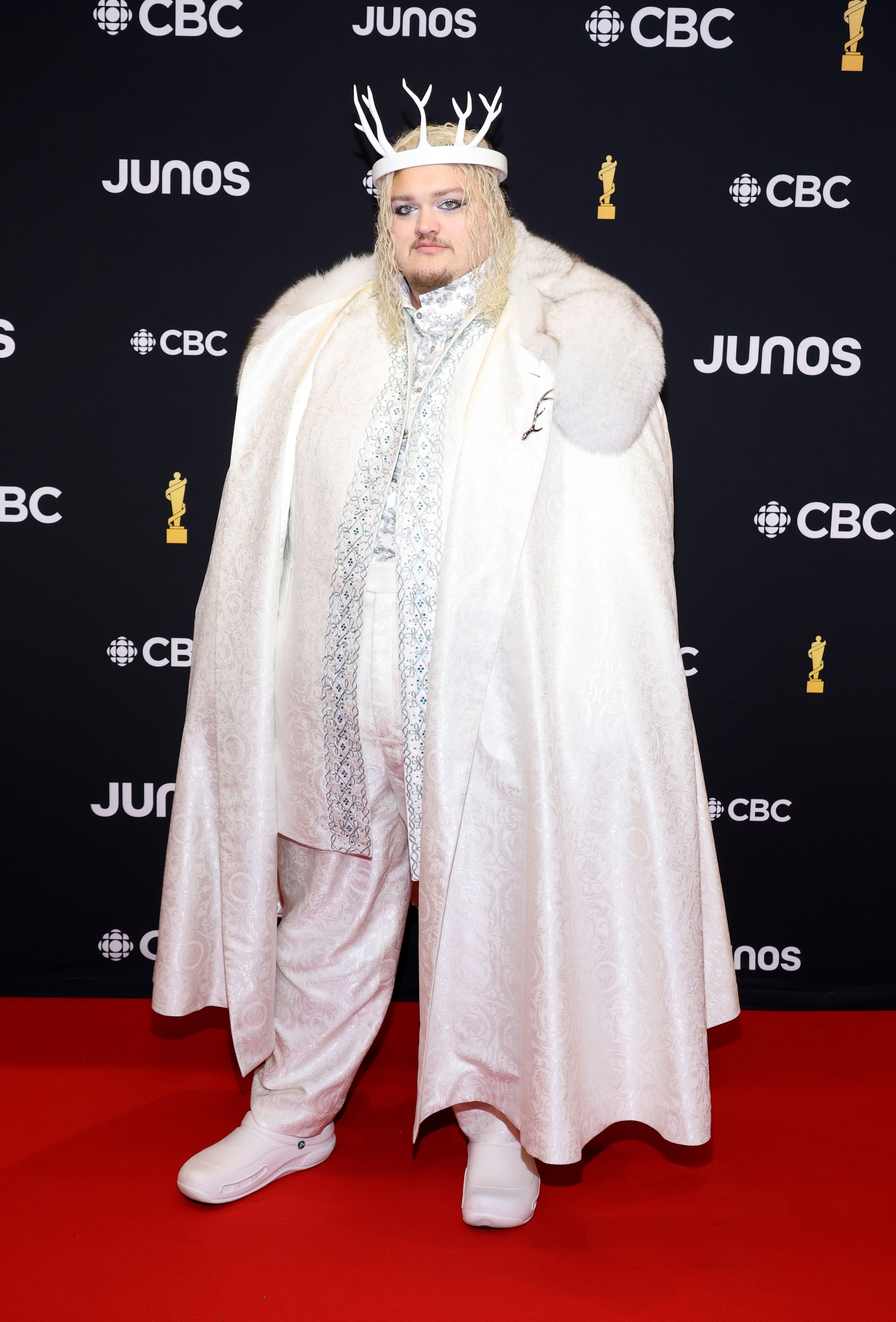 Person in regal white cape and crown posing on event backdrop