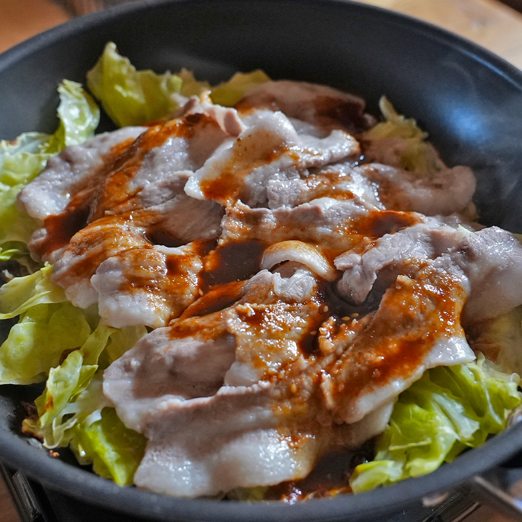 黒いボウルに入ったレタスの上に盛られた豚しゃぶとタレ。