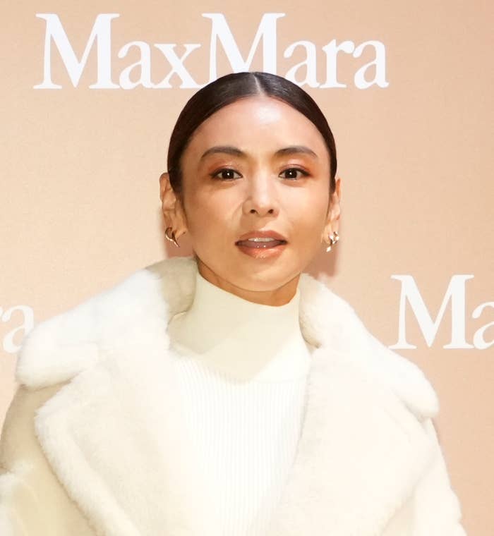 白い上着を着た女性がMaxMaraの背景前でポーズをとっています。