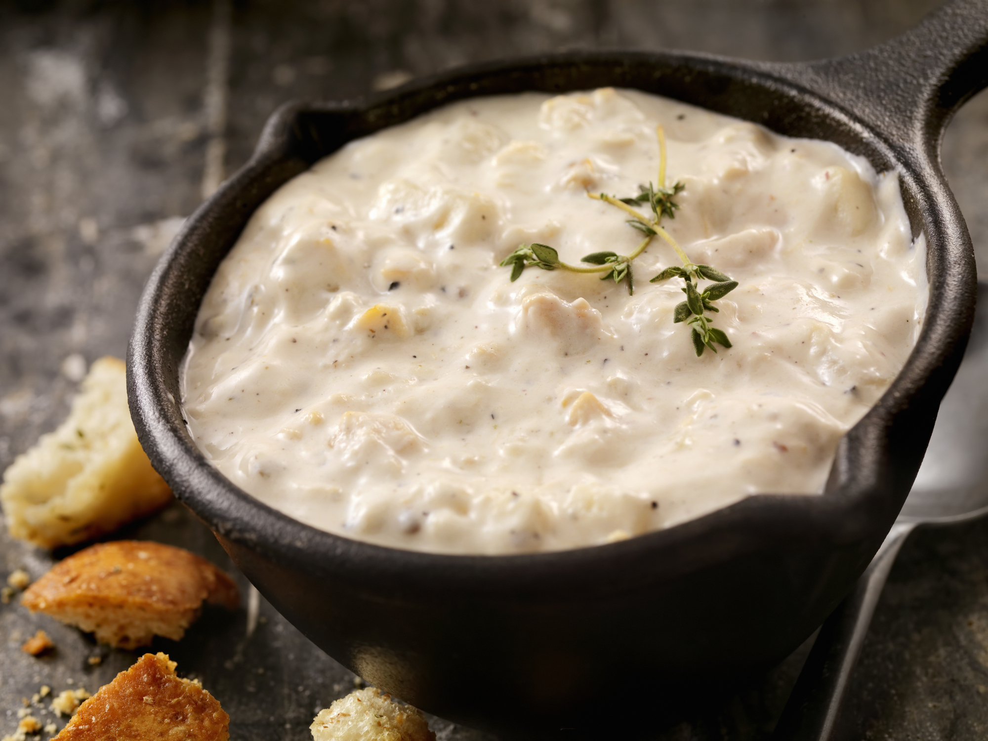 Creamy soup garnished with herbs in a black bowl, served with crumbled bread on the side