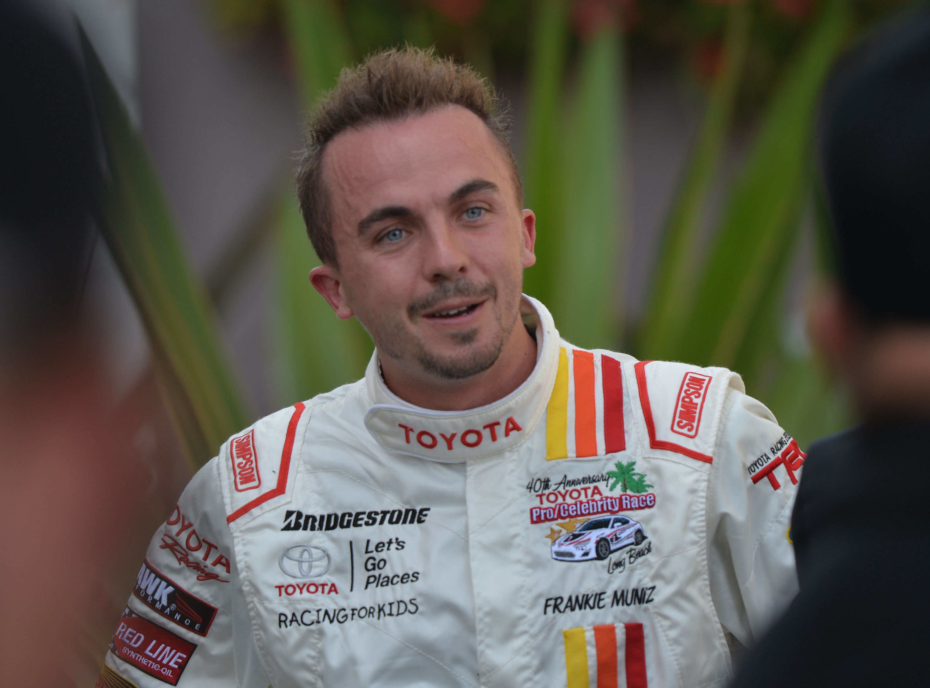 Frankie Muniz in white racing suit with Toyota and other sponsors&#x27; logos, smiling