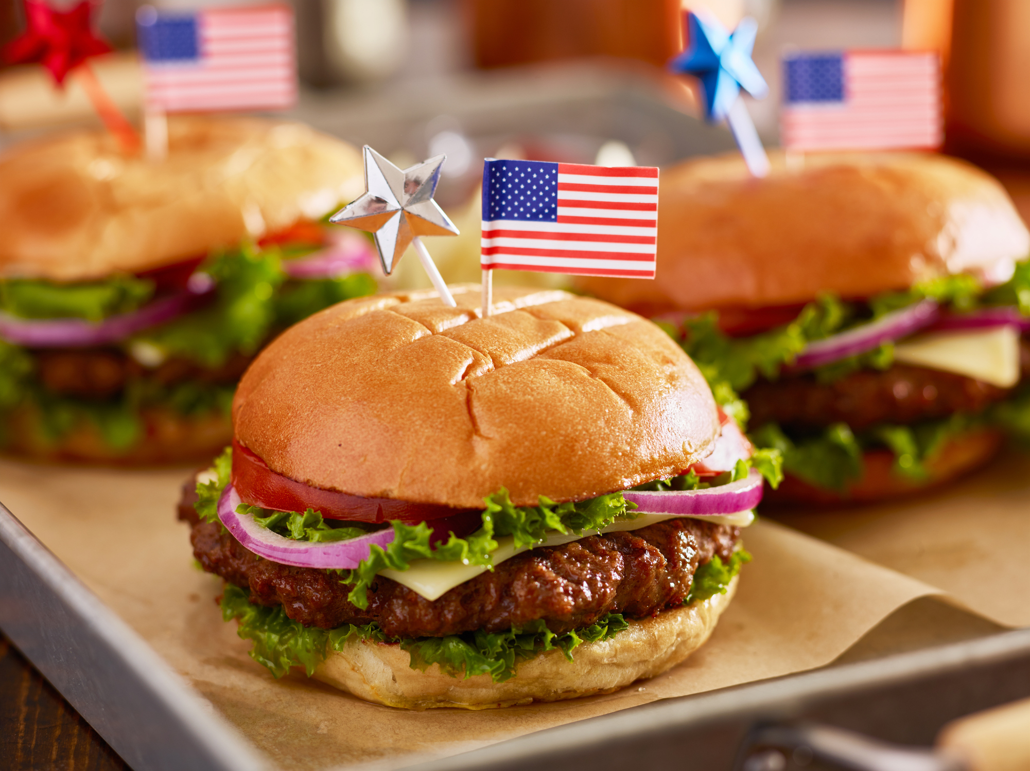 Three burgers decorated with American flags, served on a tray, in a patriotic presentation