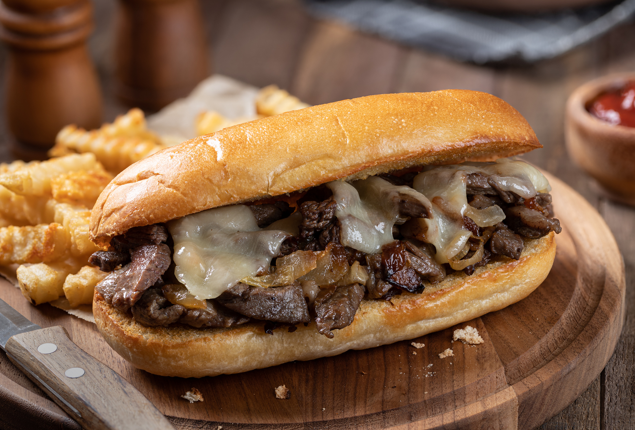 Steak and cheese sandwich on a hoagie roll with fries on a wooden board