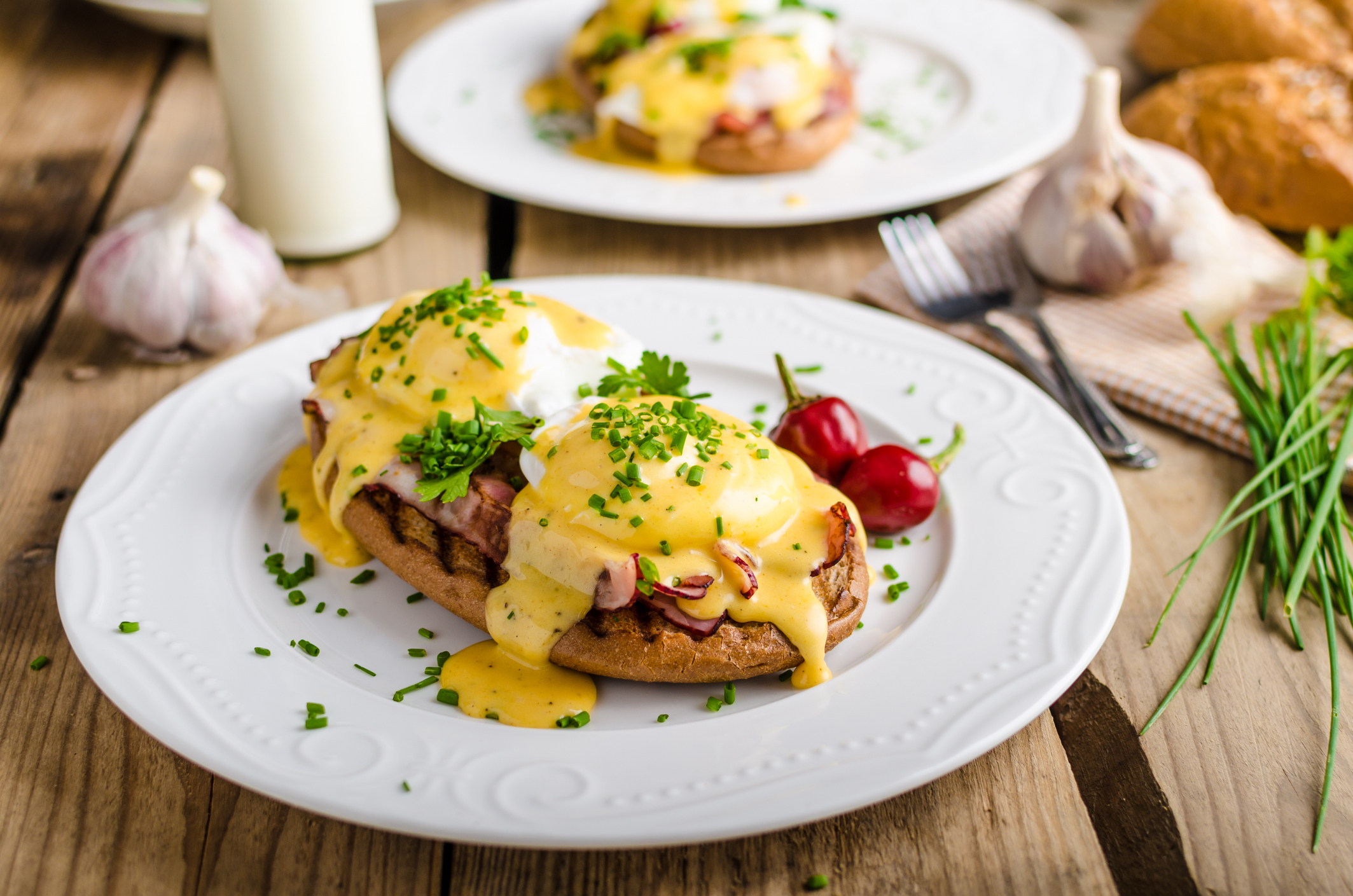 Plate with eggs Benedict and hollandaise sauce, garnished with herbs on a wooden table