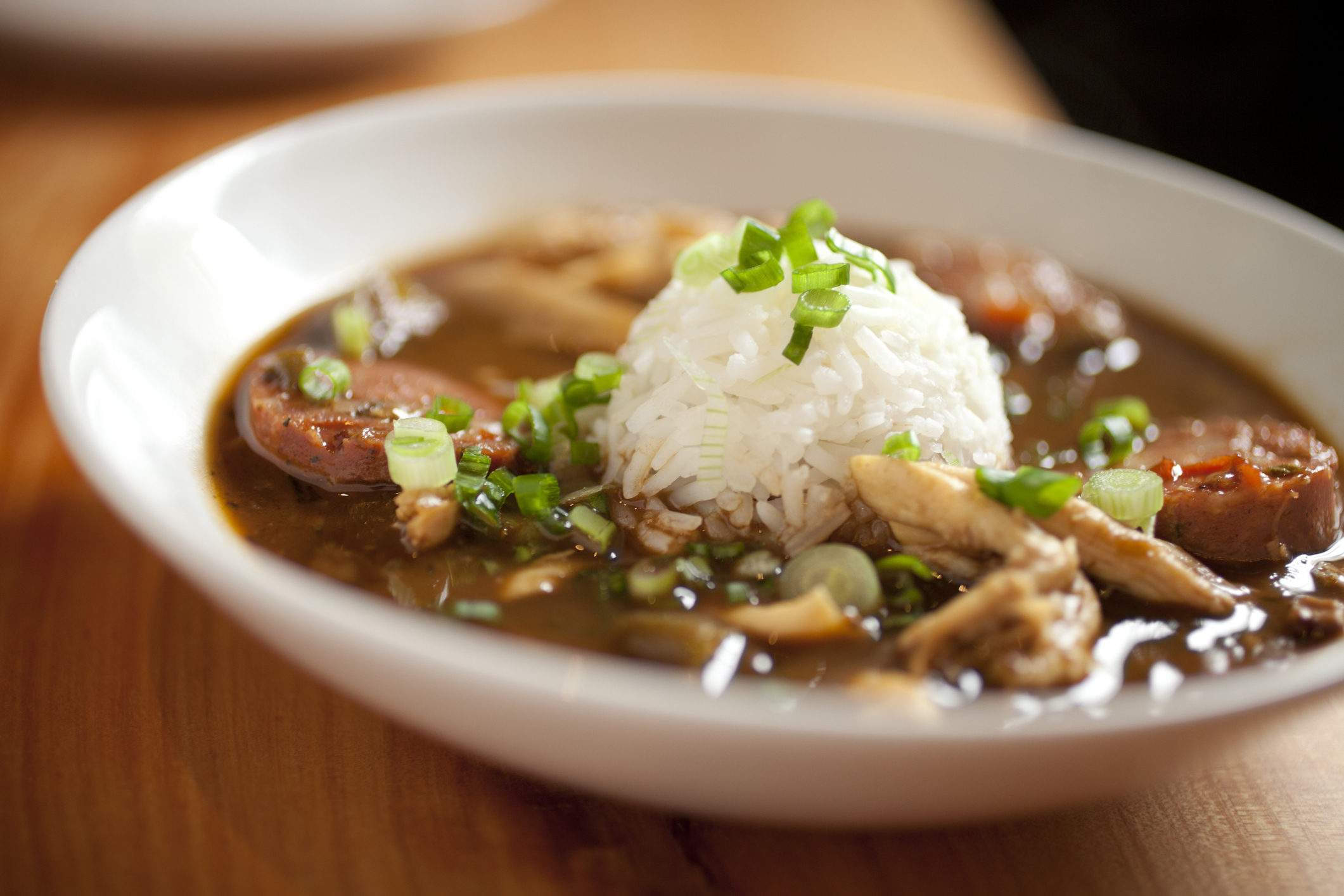 A bowl of gumbo with rice, sausage slices, and green onions