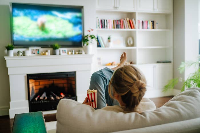 Person lounging on a sofa with popcorn, watching TV, in a cozy living room