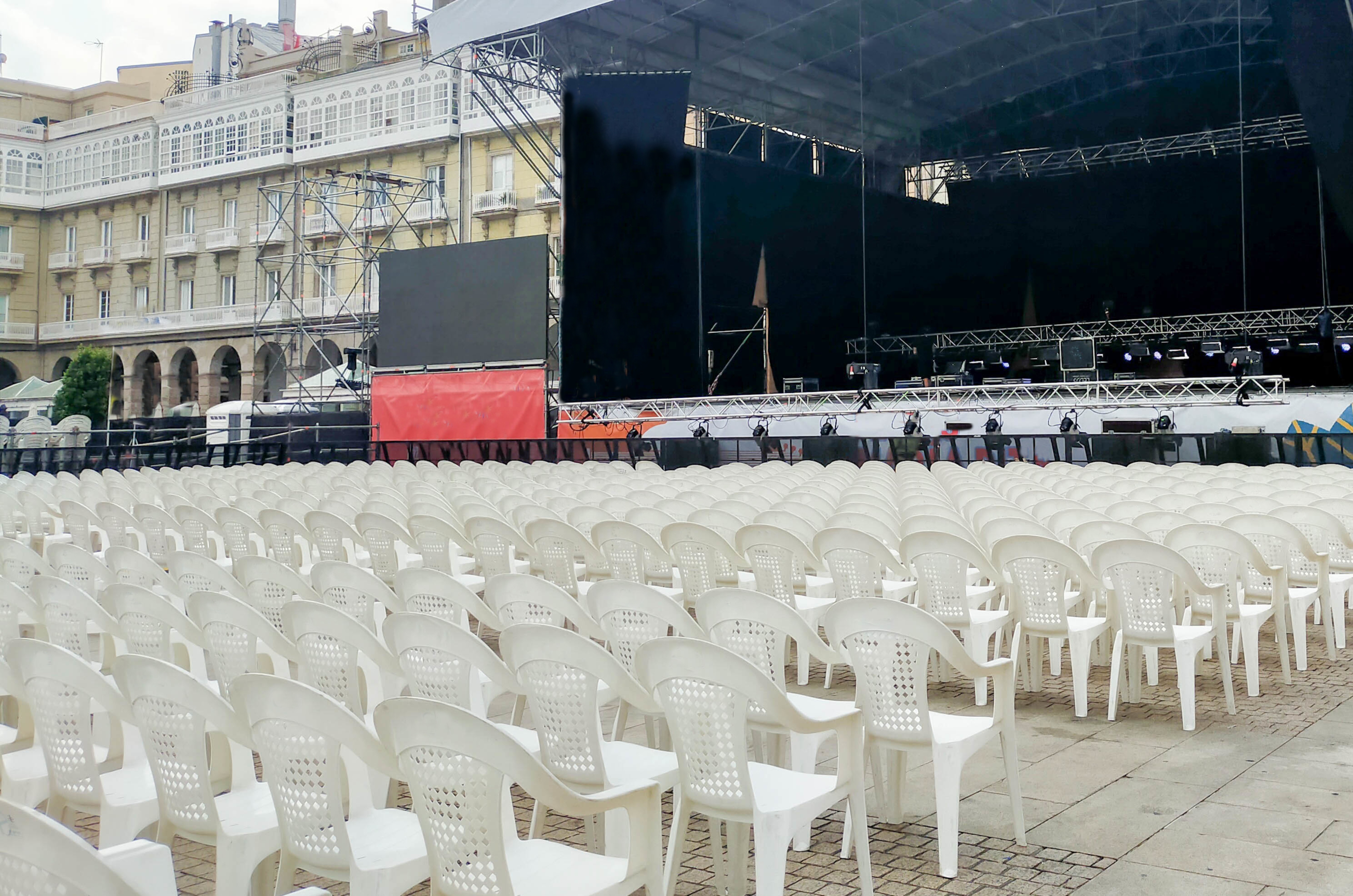 Empty white chairs set up for an outdoor event facing a large stage