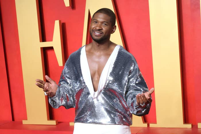 Usher posing on the red carpet in a shiny, deep V-neck top and trousers