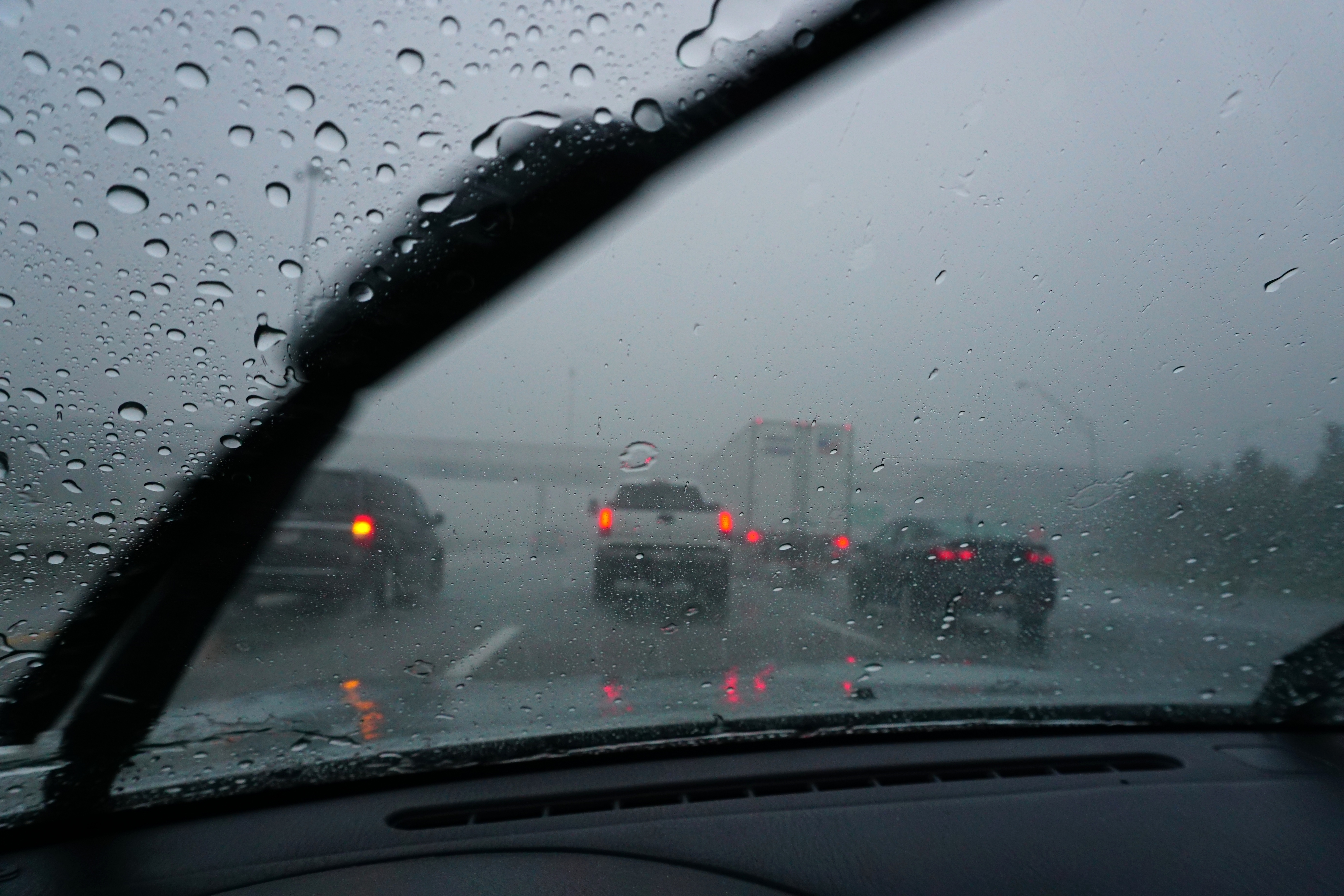 View from car&#x27;s interior with raindrops on windshield, vehicles on a rainy highway ahead